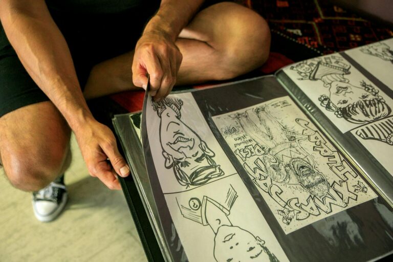 A person wearing shorts and sneakers turning pages of a comic art album, with close-up on hands and drawings.